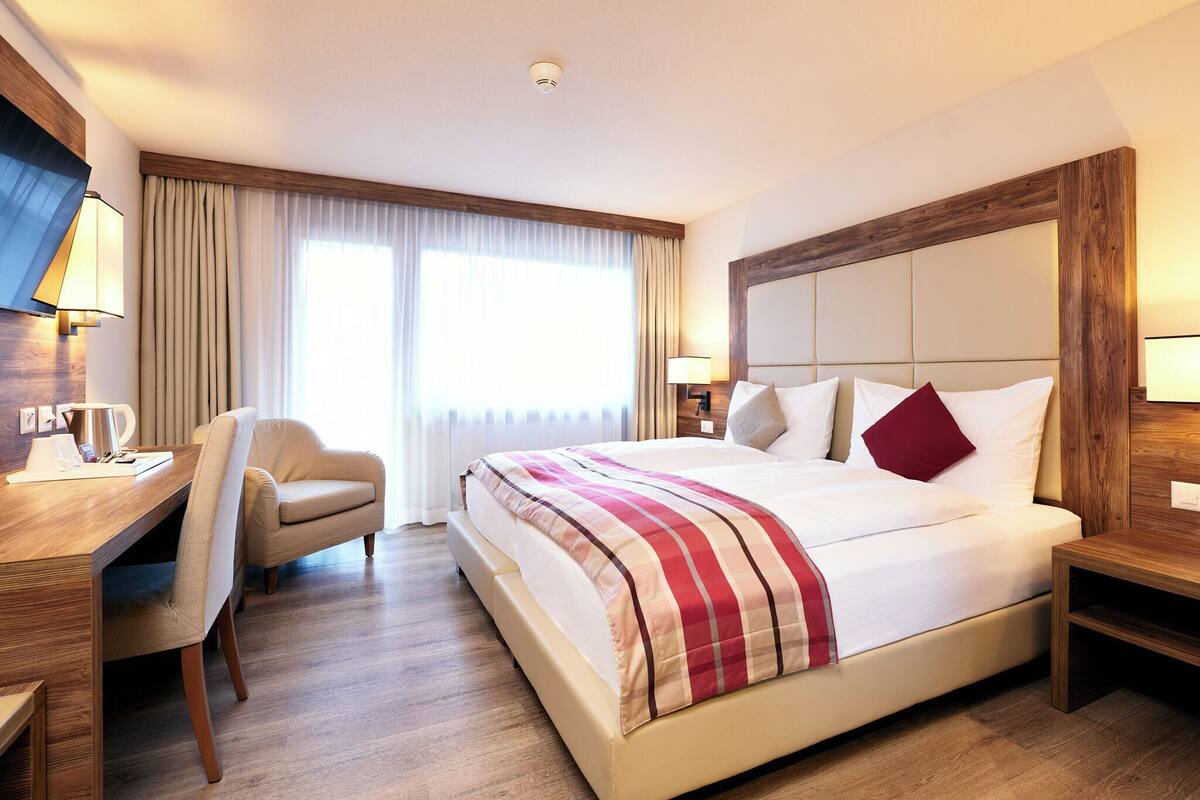 A hotel room with a large bed, a desk with a chair, a TV, and a window with curtains.