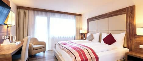 Habitación de hotel con una cama grande, un escritorio con una silla, un televisor y una ventana con cortinas.