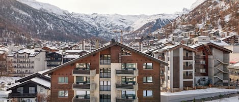 Un moderno edificio de estación de esquí con varios balcones y vistas a montañas nevadas.