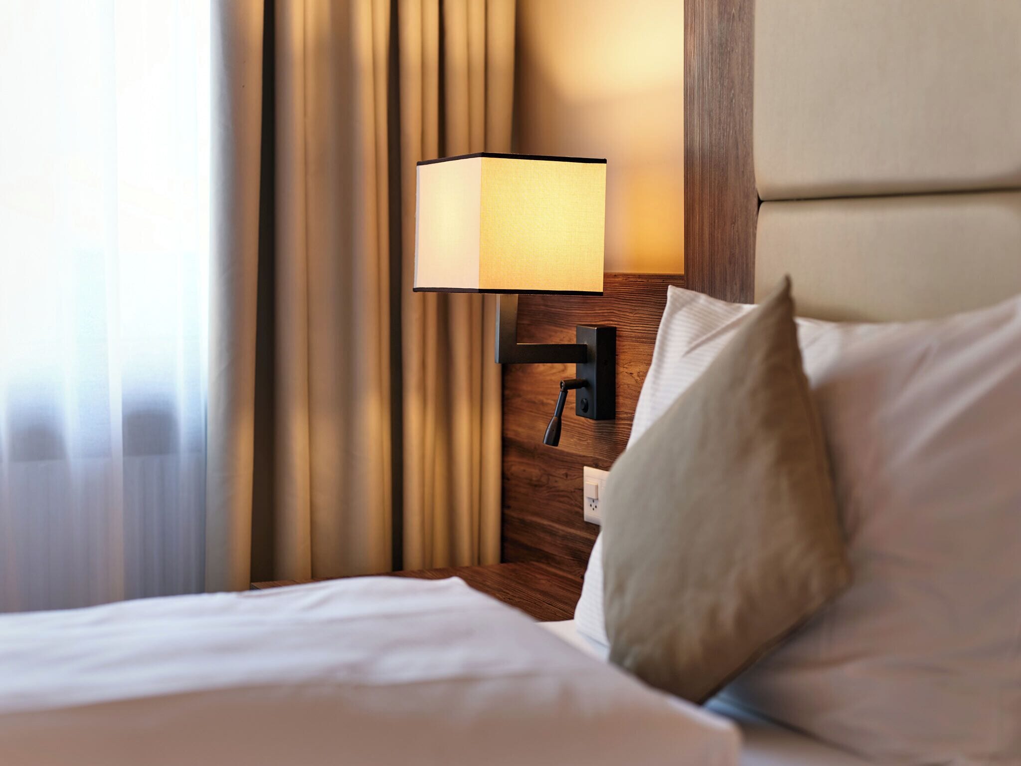 A neatly made bed with white linens, a bedside lamp, and a wooden nightstand.