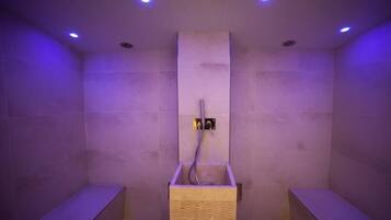 A modern shower area with a wooden bench, a wall-mounted control panel, and recessed ceiling lighting.