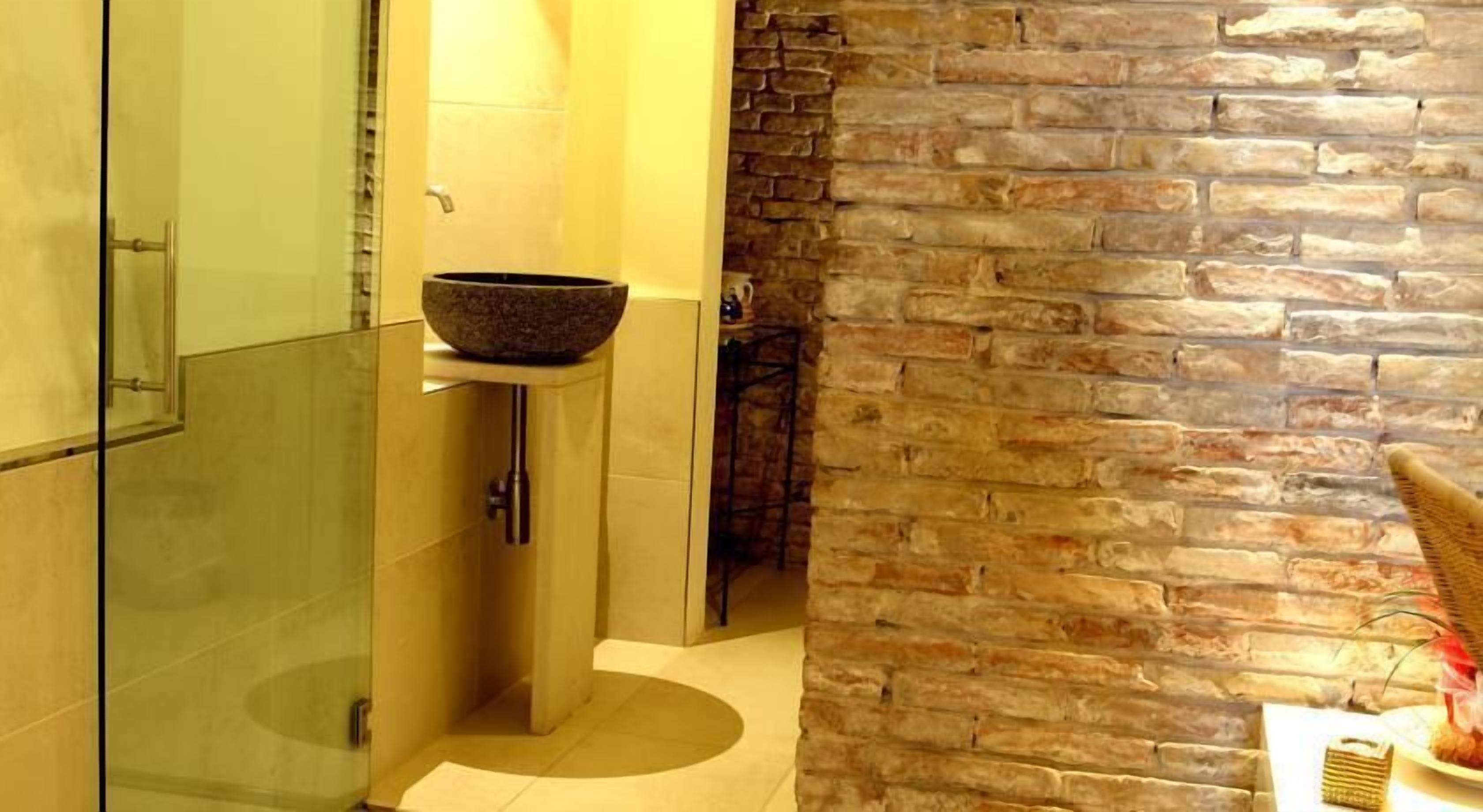 Un baño con cabina de ducha de vidrio, un lavabo de piedra y una pared de piedra.