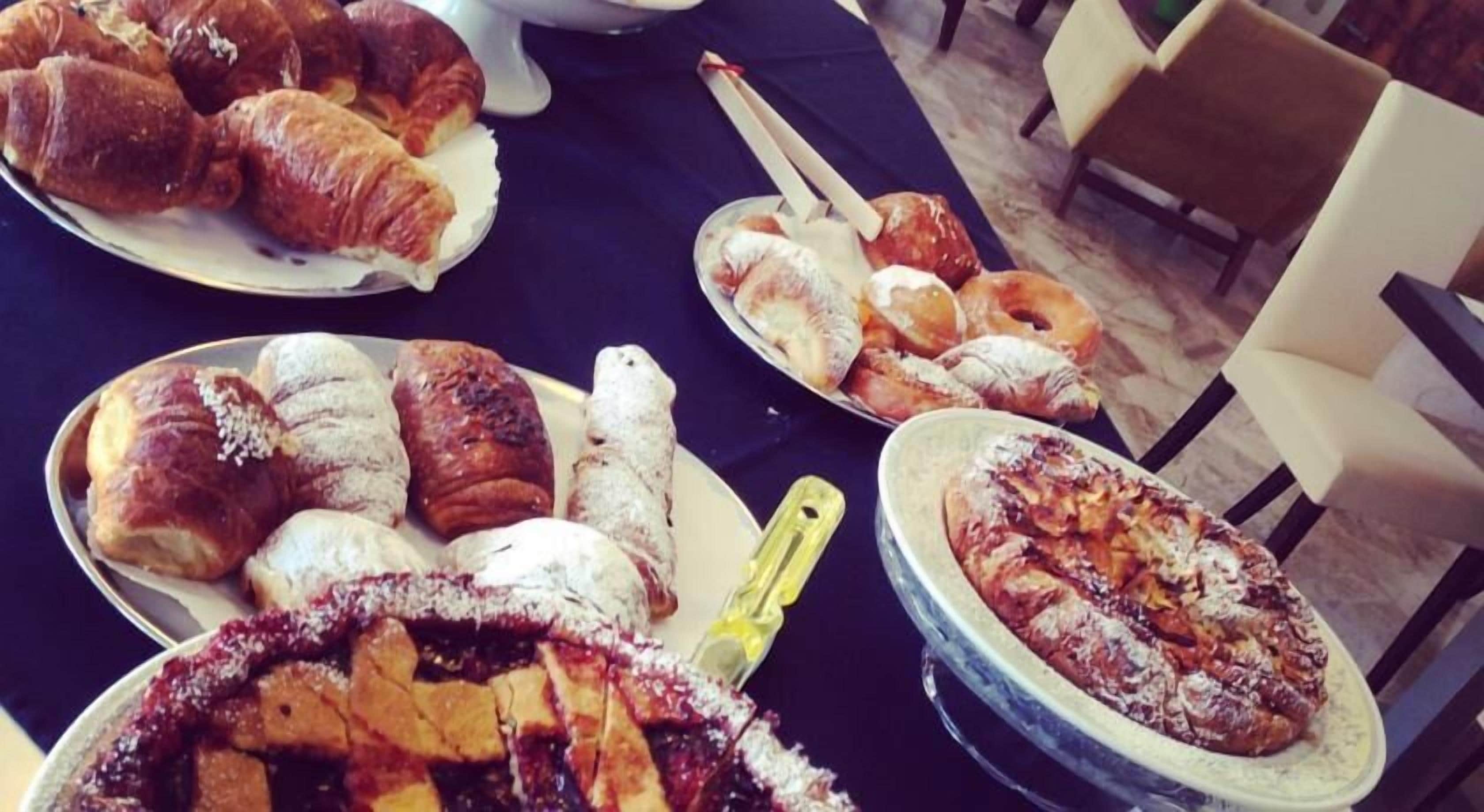 A table with various pastries and desserts, including croissants, a pie, and a cake.