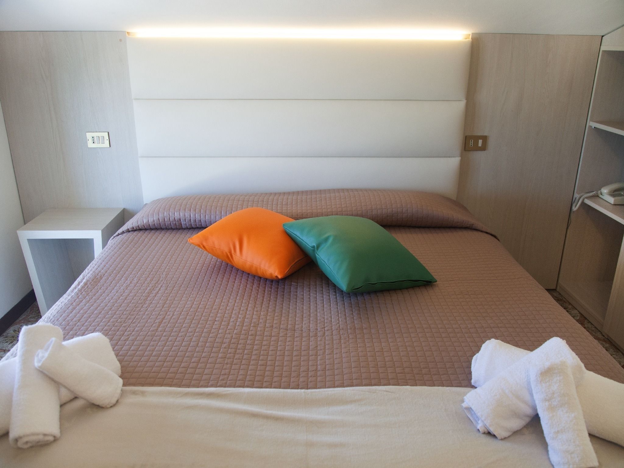 Een hotelkamer met een bed, twee kussens, een nachtkastje en een telefoon.