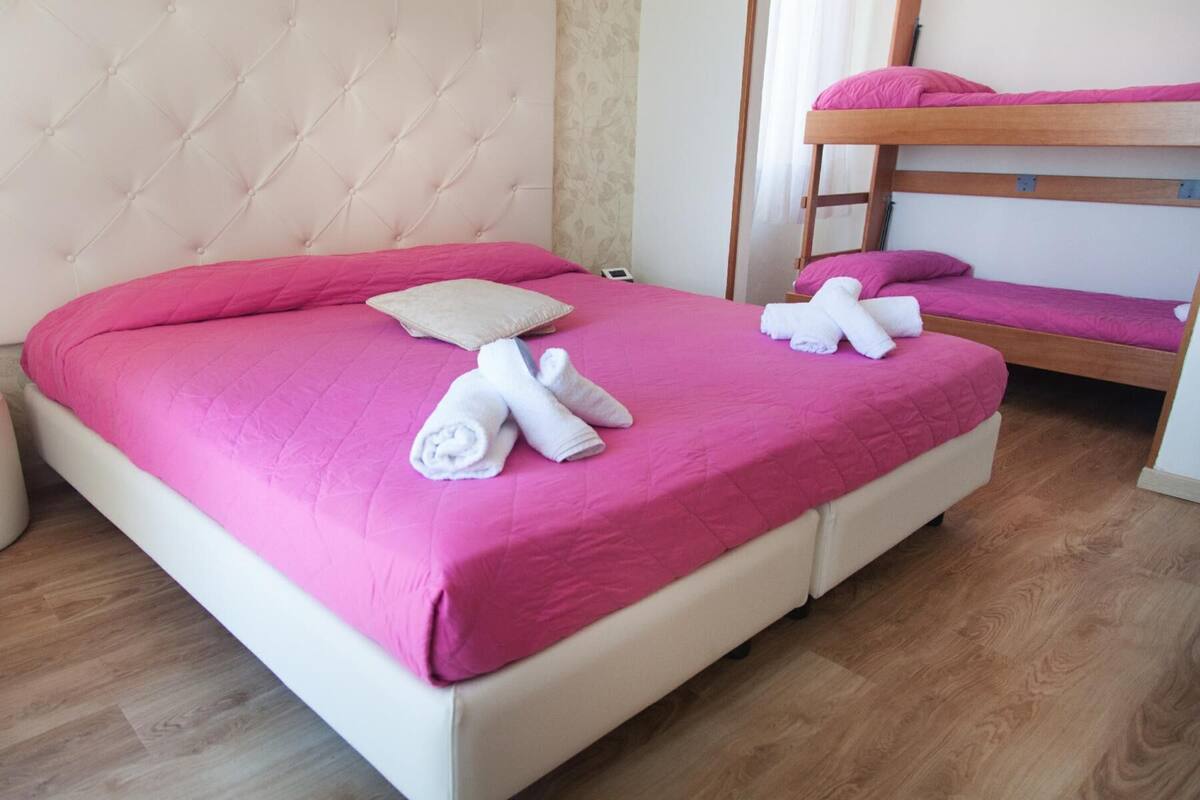 A hotel room with a single bed, a bunk bed, and a bedside table.