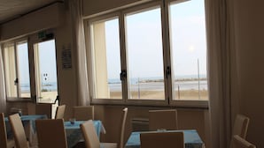 A dining area with tables and chairs, large windows with a view of the beach, and a ceiling with recessed lighting. - Riviera Mare Beach Life Hotel (Rimini)