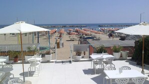 A beachside patio with white tables and chairs, umbrellas, and a view of the beach and sea. - Riviera Mare Beach Life Hotel (Rimini)