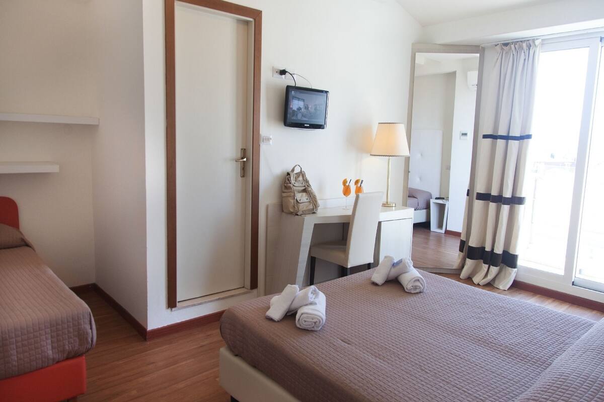 A hotel room with a bed, a desk, a chair, a TV, and a window with curtains.