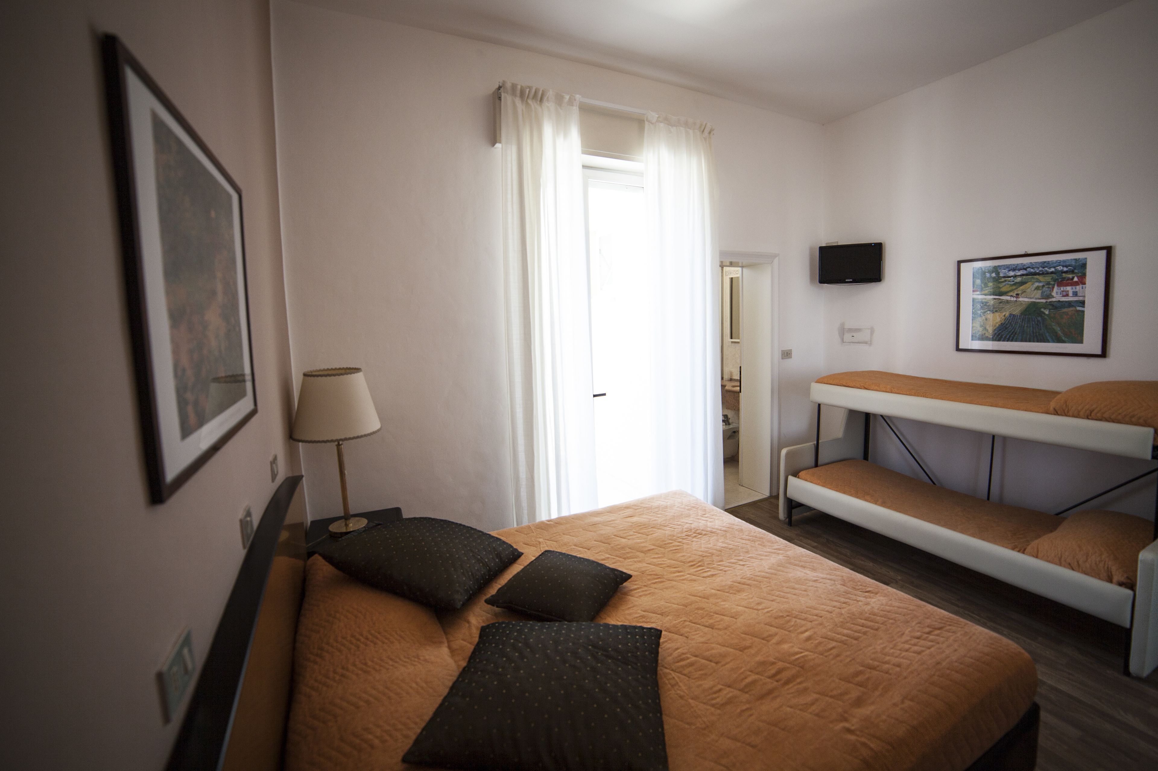 Une chambre d’hôtel avec un lit simple, un bureau, une chaise, une télévision et une fenêtre avec des rideaux.