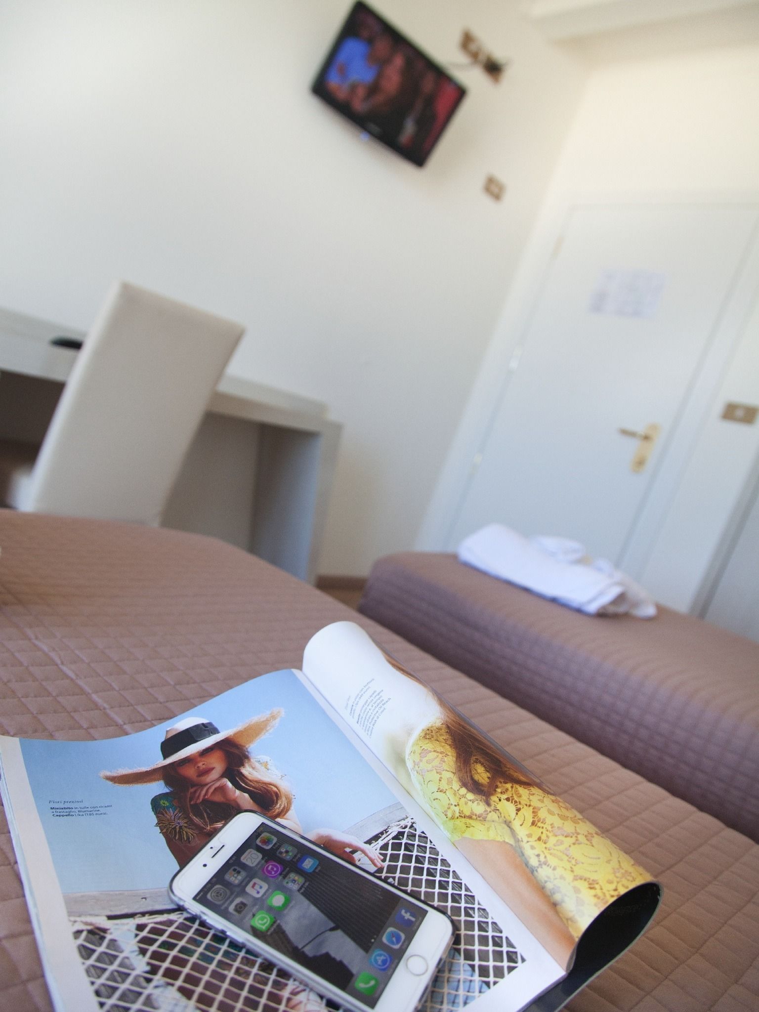 Habitación de hotel con cama, televisor en la pared, una revista sobre la cama y un teléfono inteligente encima de la revista.