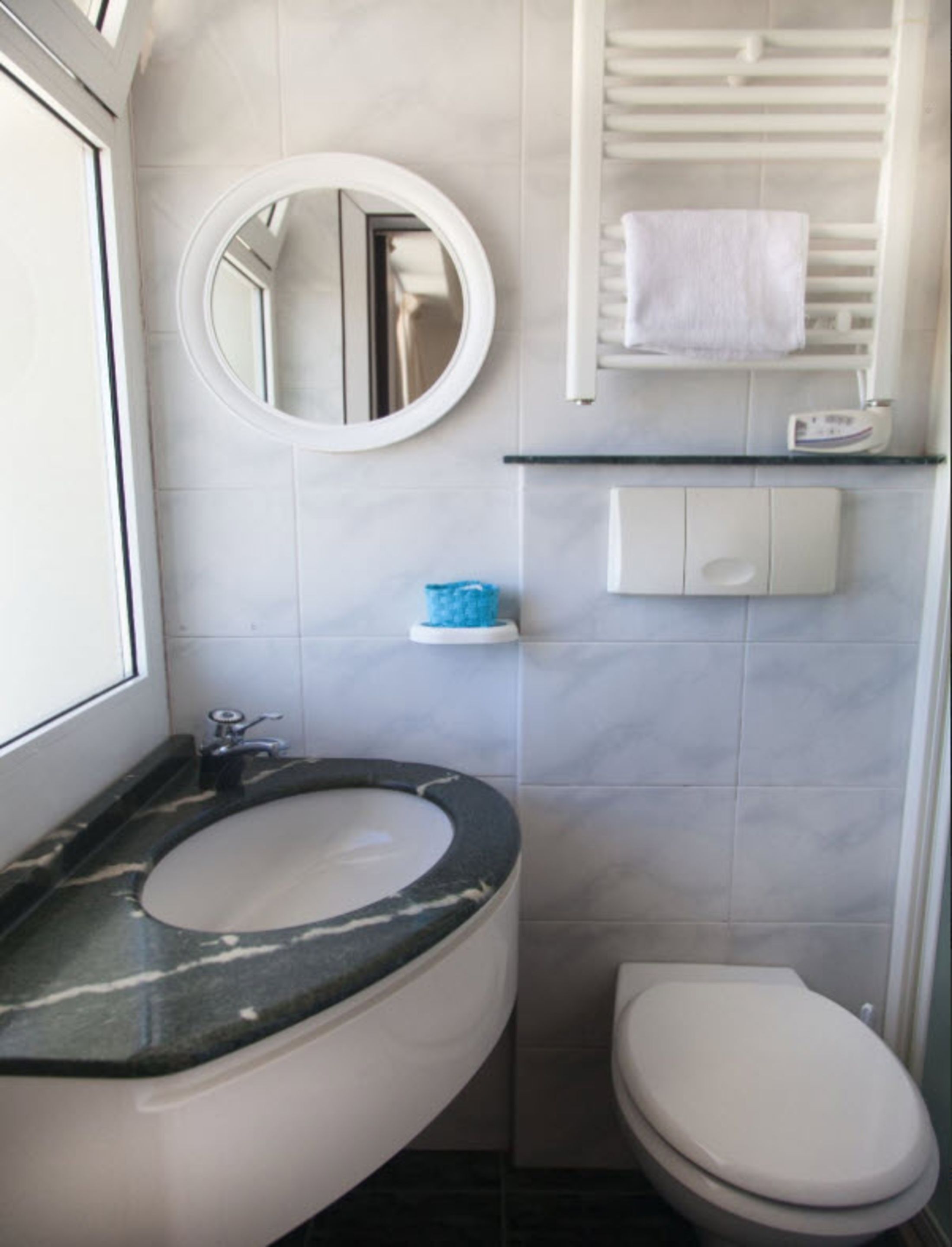 Un baño con lavamanos de mármol, inodoro, espejo y toallero.