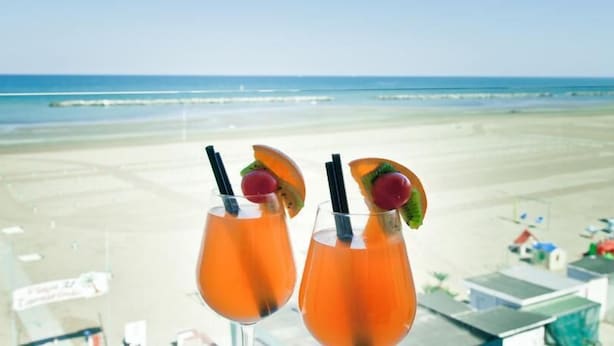 Two cocktails with fruit garnishes on a balcony overlooking a beach. - Riviera Mare Beach Life Hotel (Rimini)