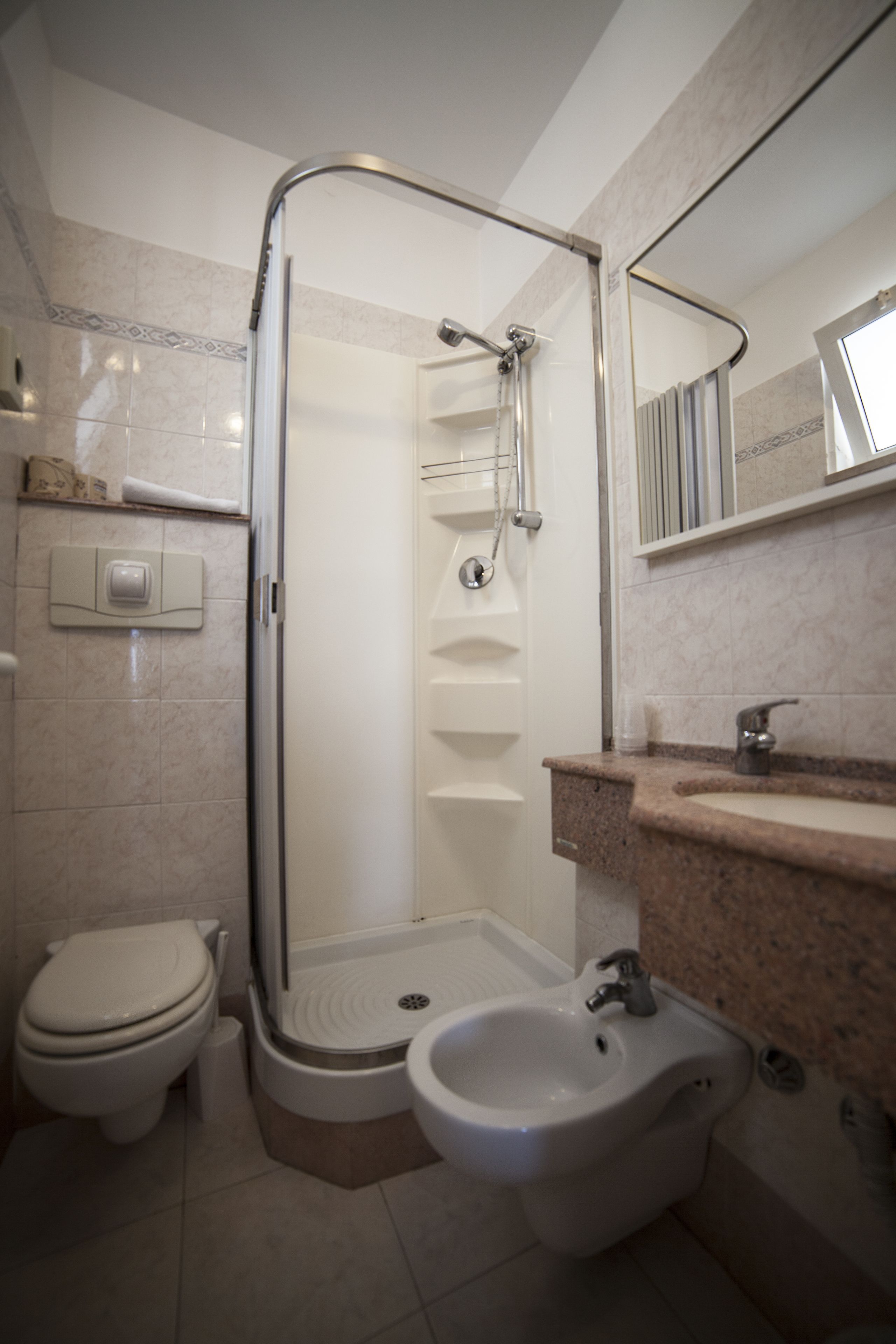 A bathroom with a shower, toilet, bidet, and a sink.