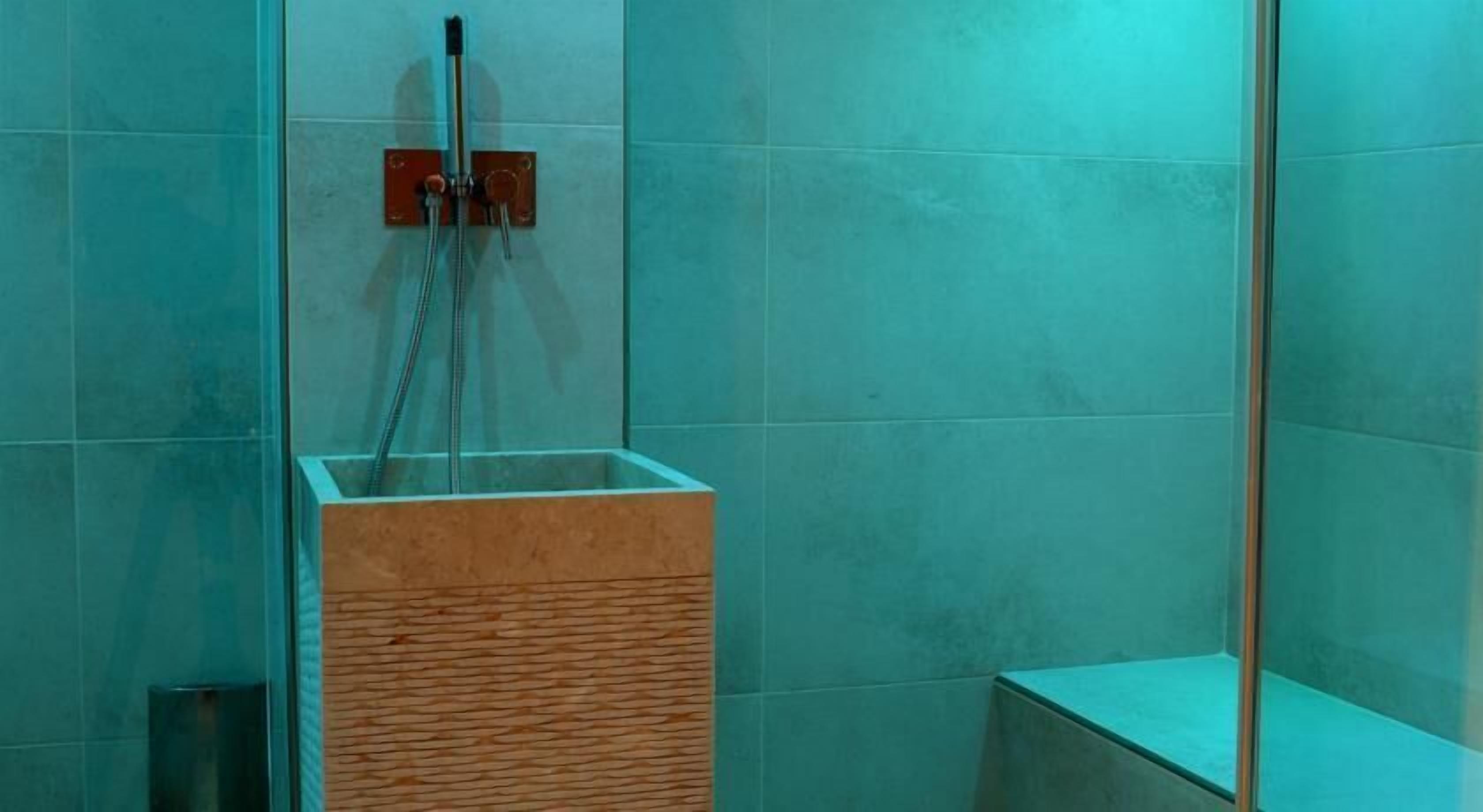 Un baño con cabina de ducha de vidrio, tocador de madera y azulejos color turquesa.