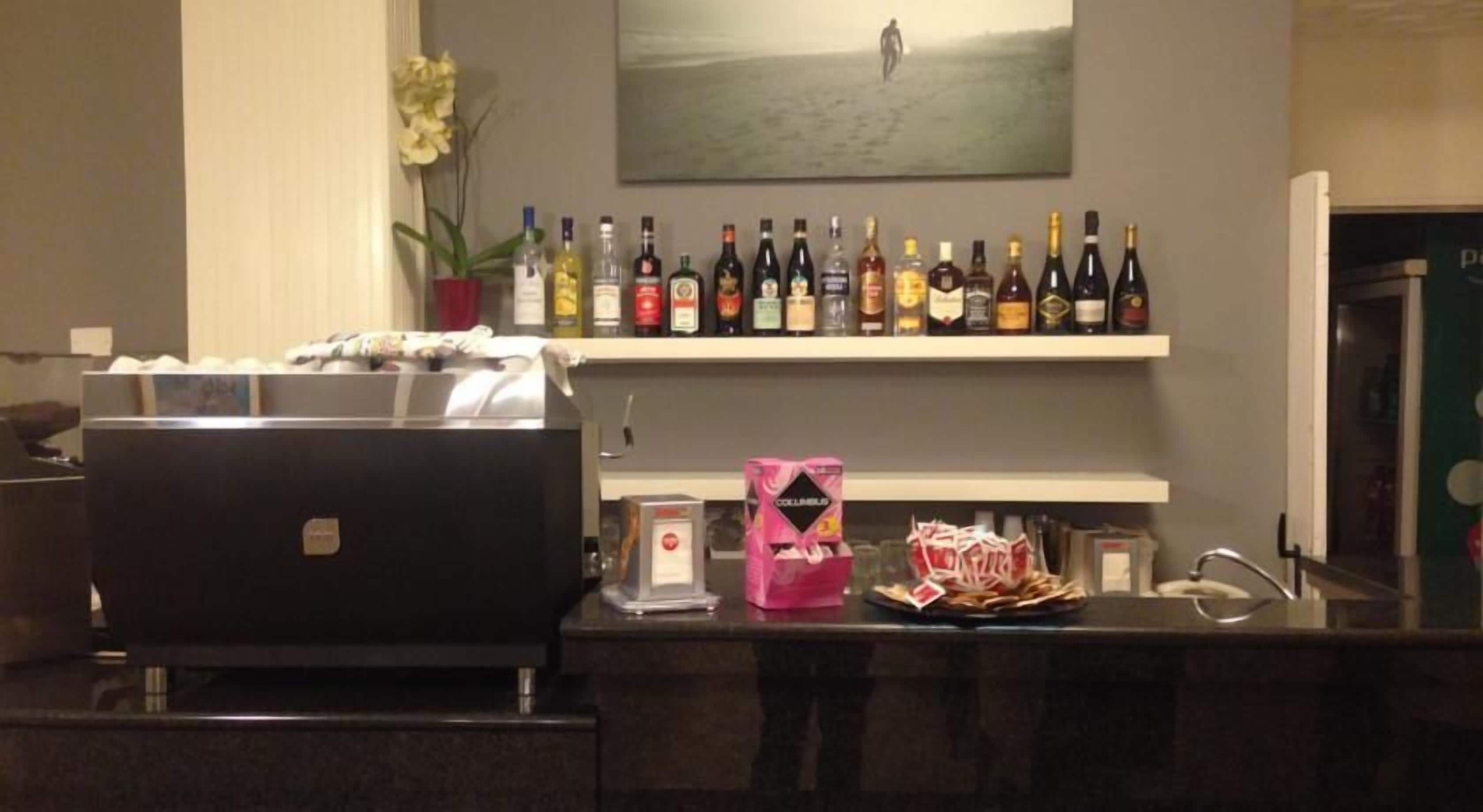 A hotel room with a minibar, a laptop, a coffee machine, and a shelf with various bottles.