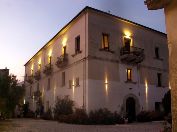 A building with multiple balconies and windows, surrounded by a gravel courtyard and some plants. - Hotel Castello dei Principi (Capaccio-Paestum)