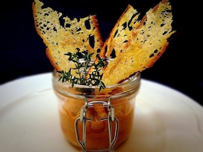 A glass jar with a metal clasp containing a dark liquid, possibly a sauce or dressing, with pieces of toasted bread and fresh herbs on top. - Hotel Castello dei Principi (Capaccio-Paestum)