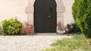 Un bâtiment doté d’une entrée arquée sombre, d’une petite fenêtre au-dessus et de plantes en pot disposées autour de l’entrée.