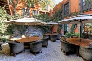 An outdoor patio area with wicker furniture and umbrellas, surrounded by stone flooring and greenery.
