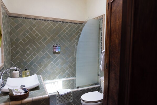 A bathroom with a tiled shower, a sink with toiletries, and a toilet.