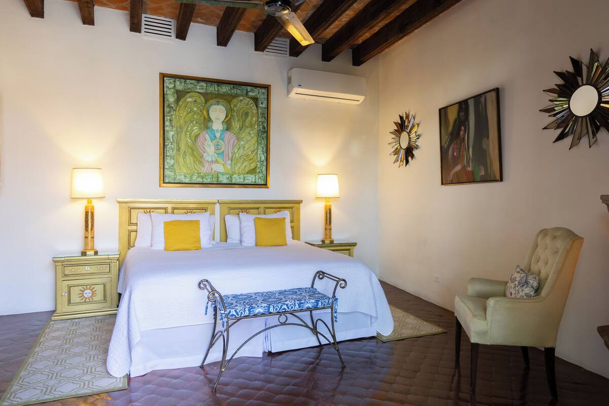 Ein Schlafzimmer mit Bett, Nachttischlampen, einem Sessel und Kunstwerken an den Wänden.