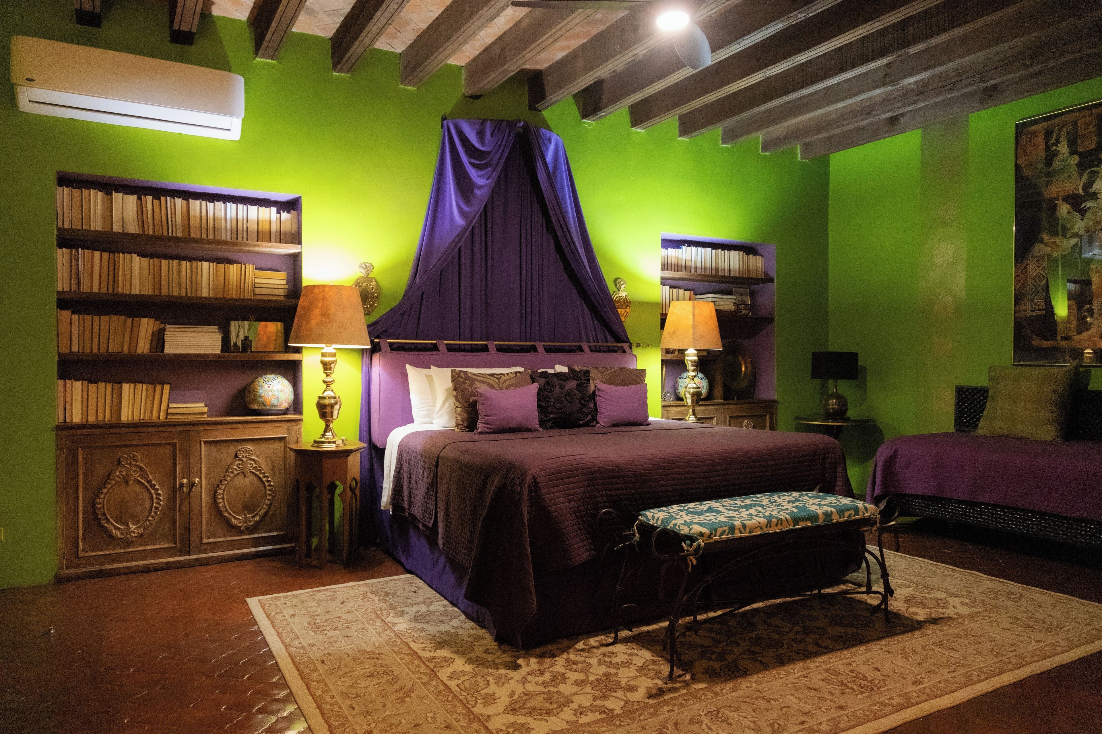 Quarto com uma cama grande, um banquinho, uma estante de livros e um ventilador de teto.