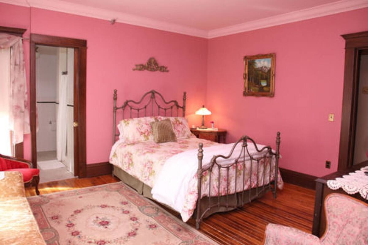 A pink-themed bedroom with a bed, bedside table, lamp, and a framed picture on the wall.