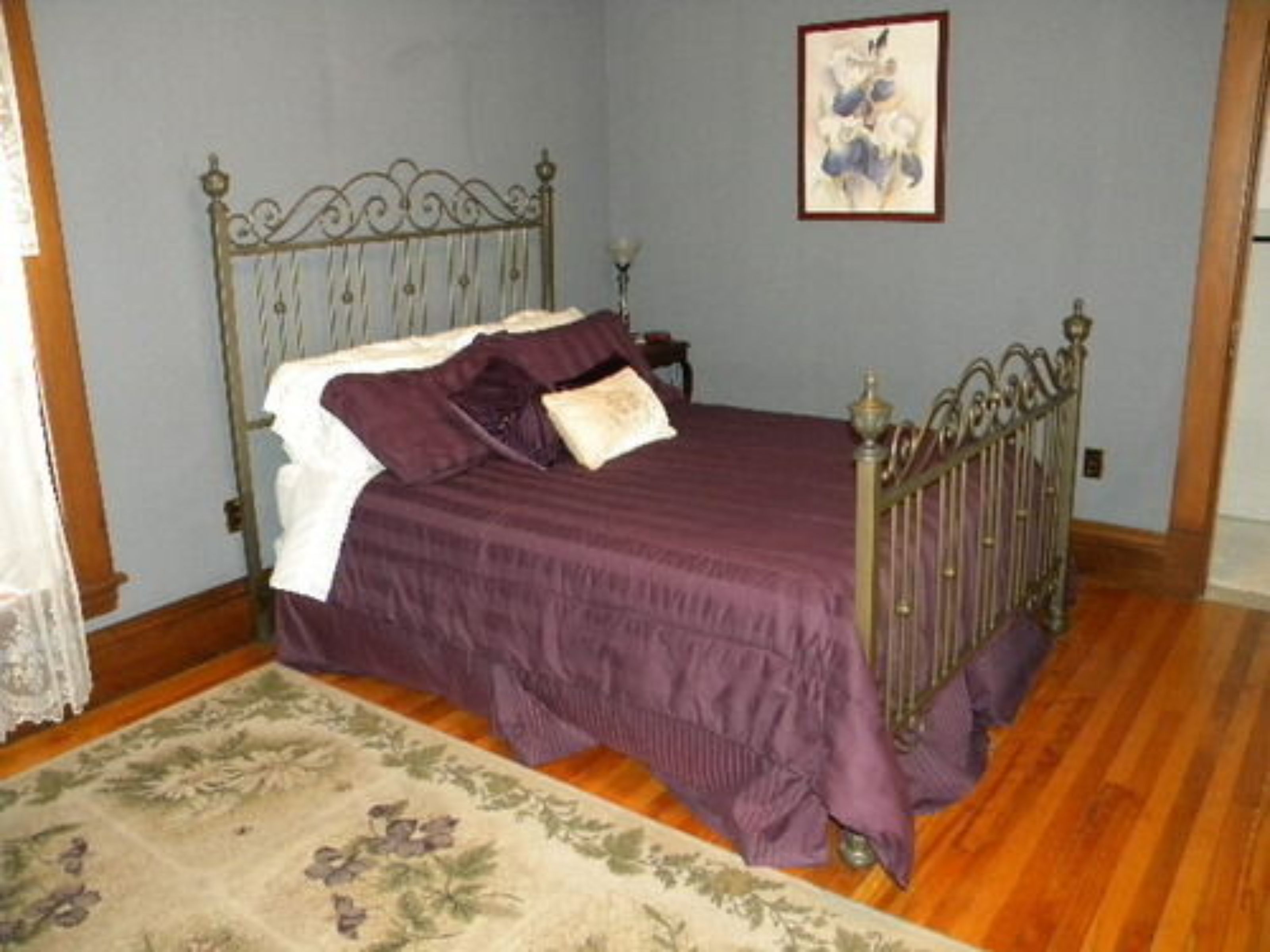 A bedroom with a metal bed frame, a purple bedspread, and a floral-patterned rug.