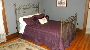 A bedroom with a metal bed frame, a purple bedspread, and a floral-patterned rug.