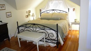 Une chambre à coucher avec un lit à baldaquin, une table de chevet, une petite table de nuit et une petite table ornée d’une plante.
