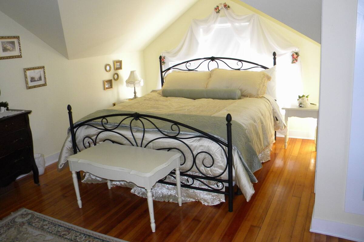A bedroom with a four-poster bed, a bedside table, a nightstand, and a small table with a plant.