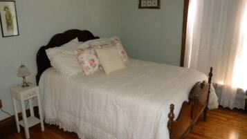 A bedroom with a wooden bed, white bedding, a nightstand with a lamp, and a window with curtains.