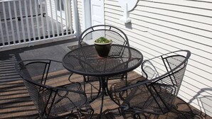 Une terrasse avec une table et des chaises rondes en métal, une plante en pot et une porte blanche avec une fenêtre.