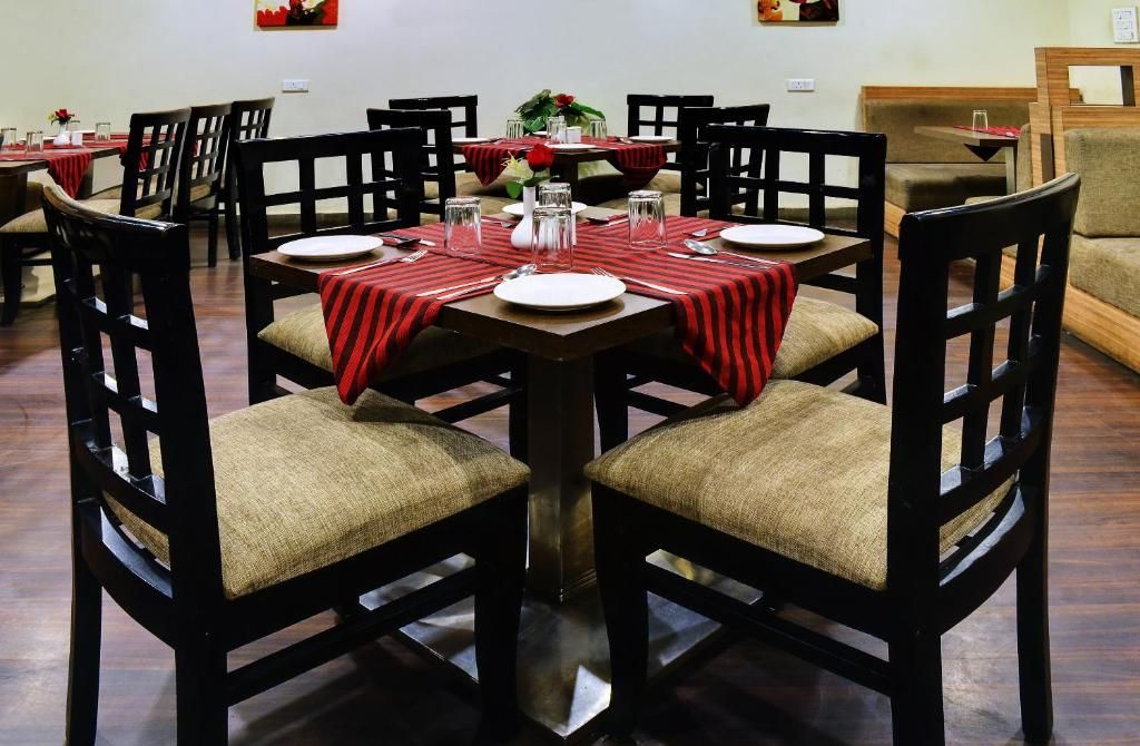 Uma área de refeições com mesas redondas, cadeiras e toalhas de mesa listradas de vermelho.