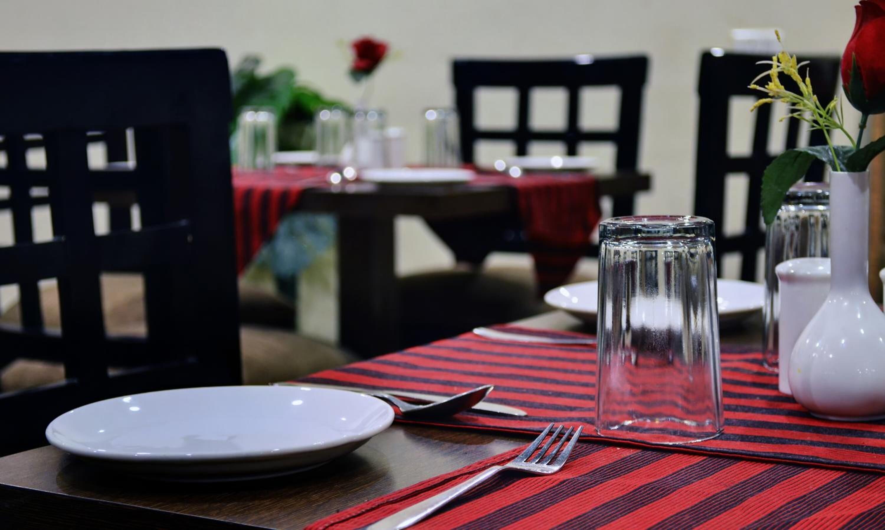 A dining table set with a plate, fork, and glass, with a red and black striped table runner.