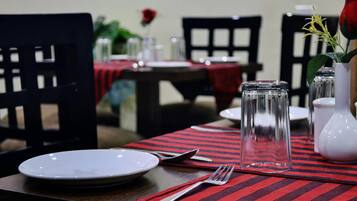 A dining table set with a plate, fork, and glass, with a red and black striped table runner.