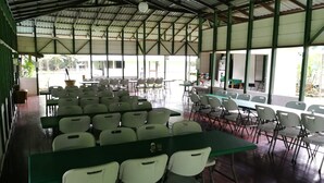 A covered dining area with tables and chairs, large windows, and a high ceiling.
