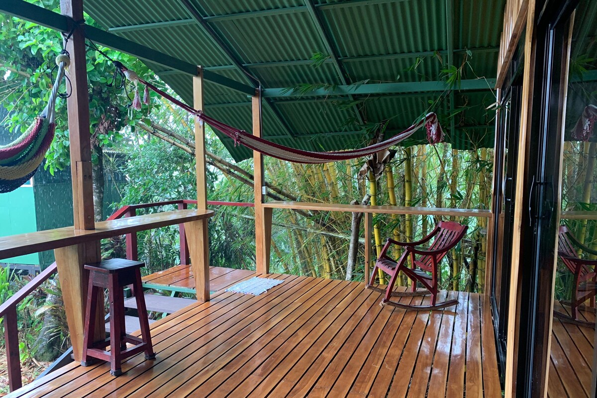 A wooden deck with a hammock, chairs, and a table.
