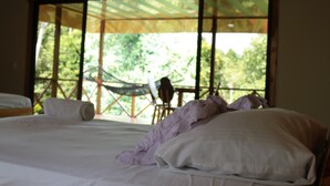 A bedroom with a large bed, a window with a view of greenery, and a hammock outside.