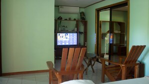 A room with a television, wooden chairs, a small table, and shelves with decorative items.