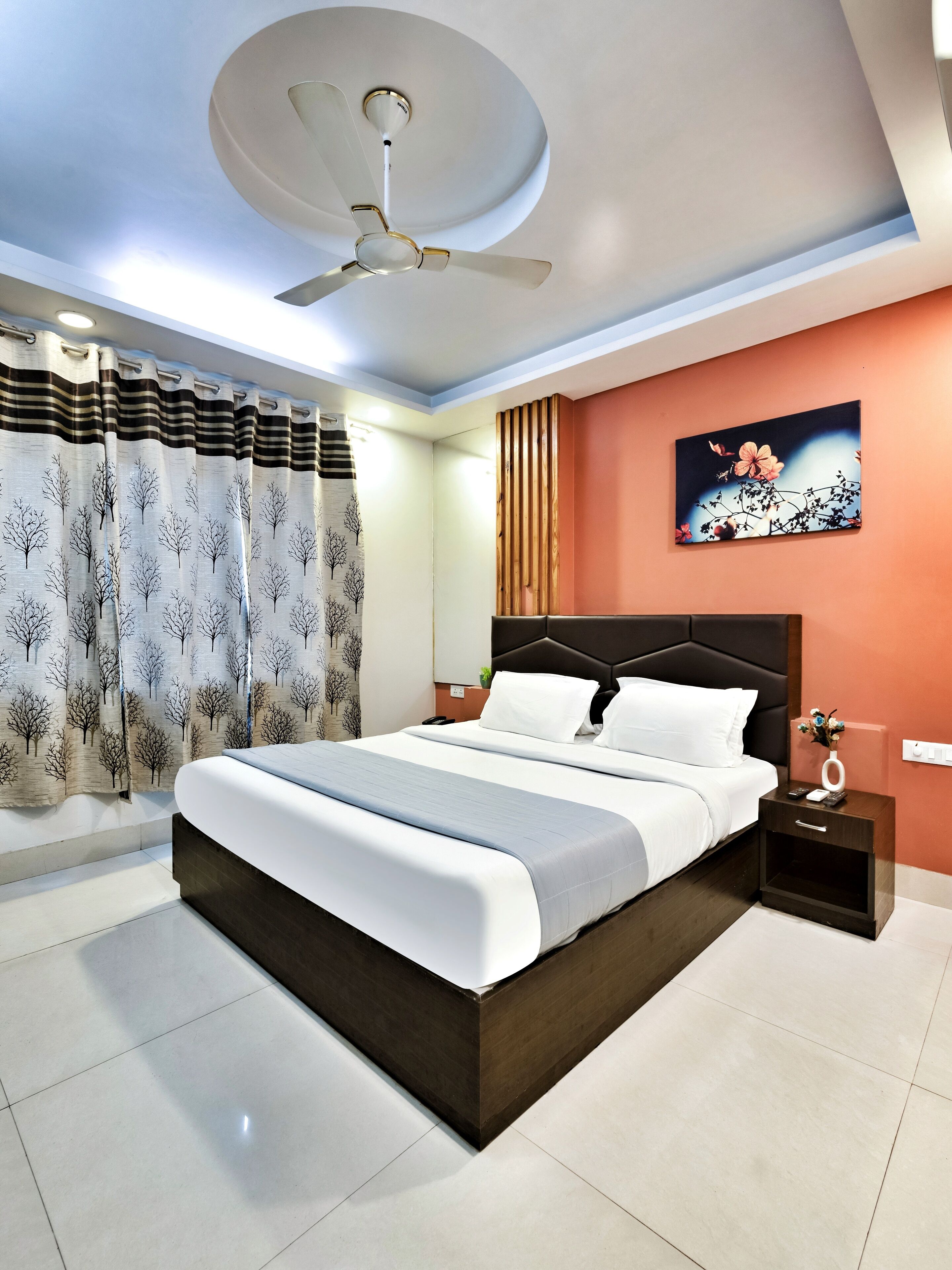 A modern bedroom with a large bed, a ceiling fan, a nightstand with a phone, and a painting on the wall.