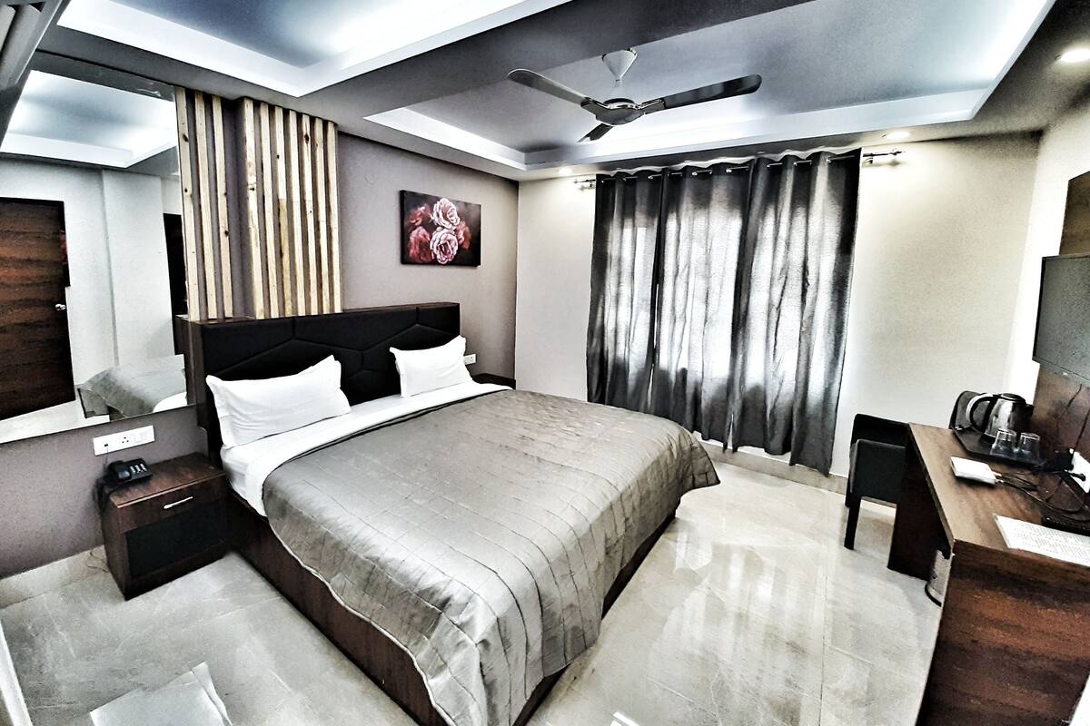 A modern bedroom with a large bed, a desk, a chair, a ceiling fan, and a painting on the wall.