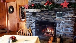 A dining area with a stone fireplace, wooden walls, and a table set for two.