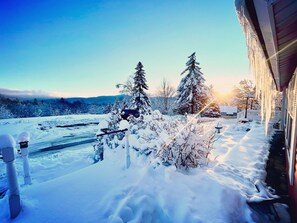 A snowy landscape with a house, snow-covered trees, and a clear sky.