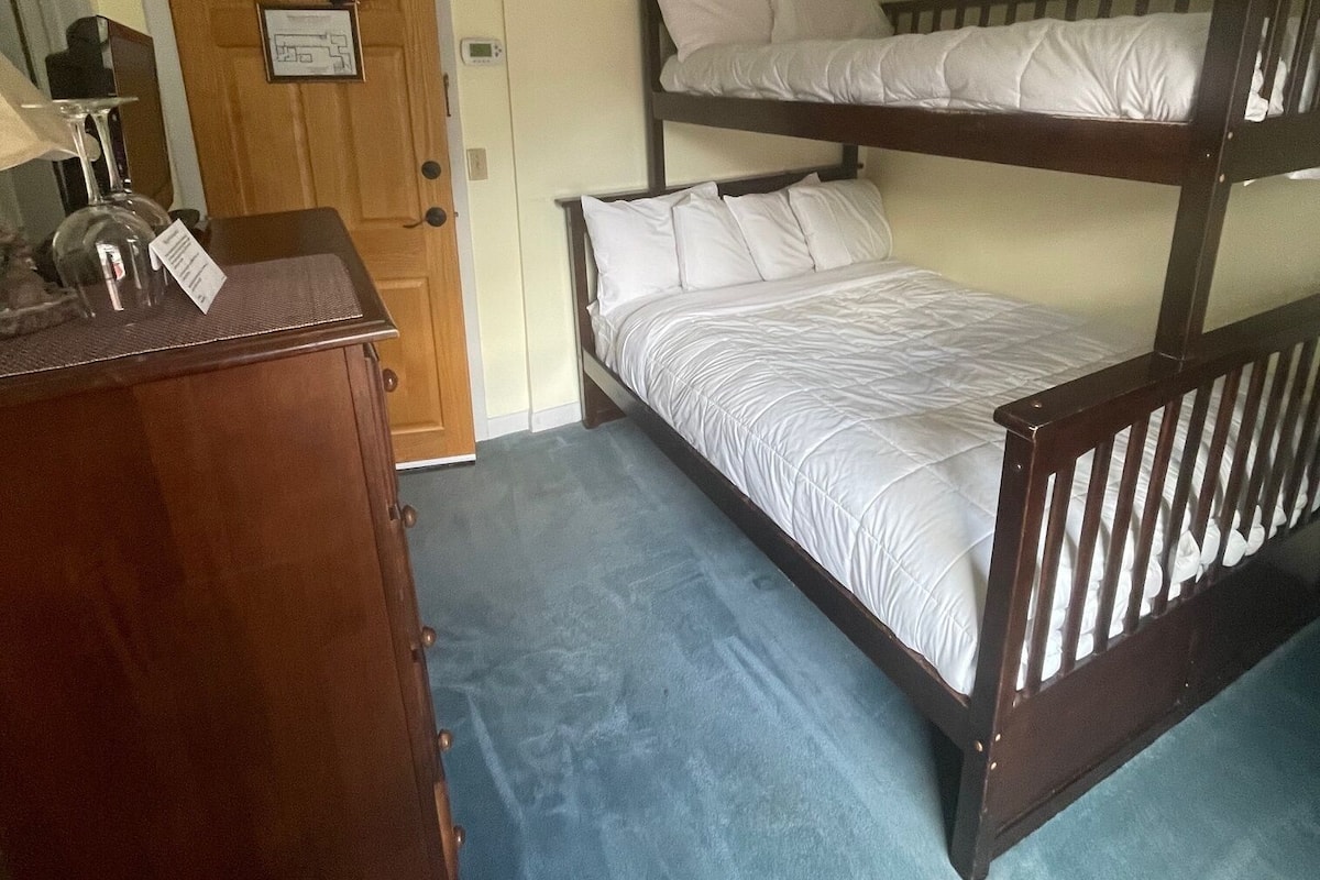 Quarto com beliche, cômoda de madeira e porta com um aviso.
