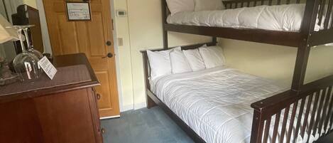 Une chambre avec un lit superposé, une commode en bois et une porte avec une pancarte.
