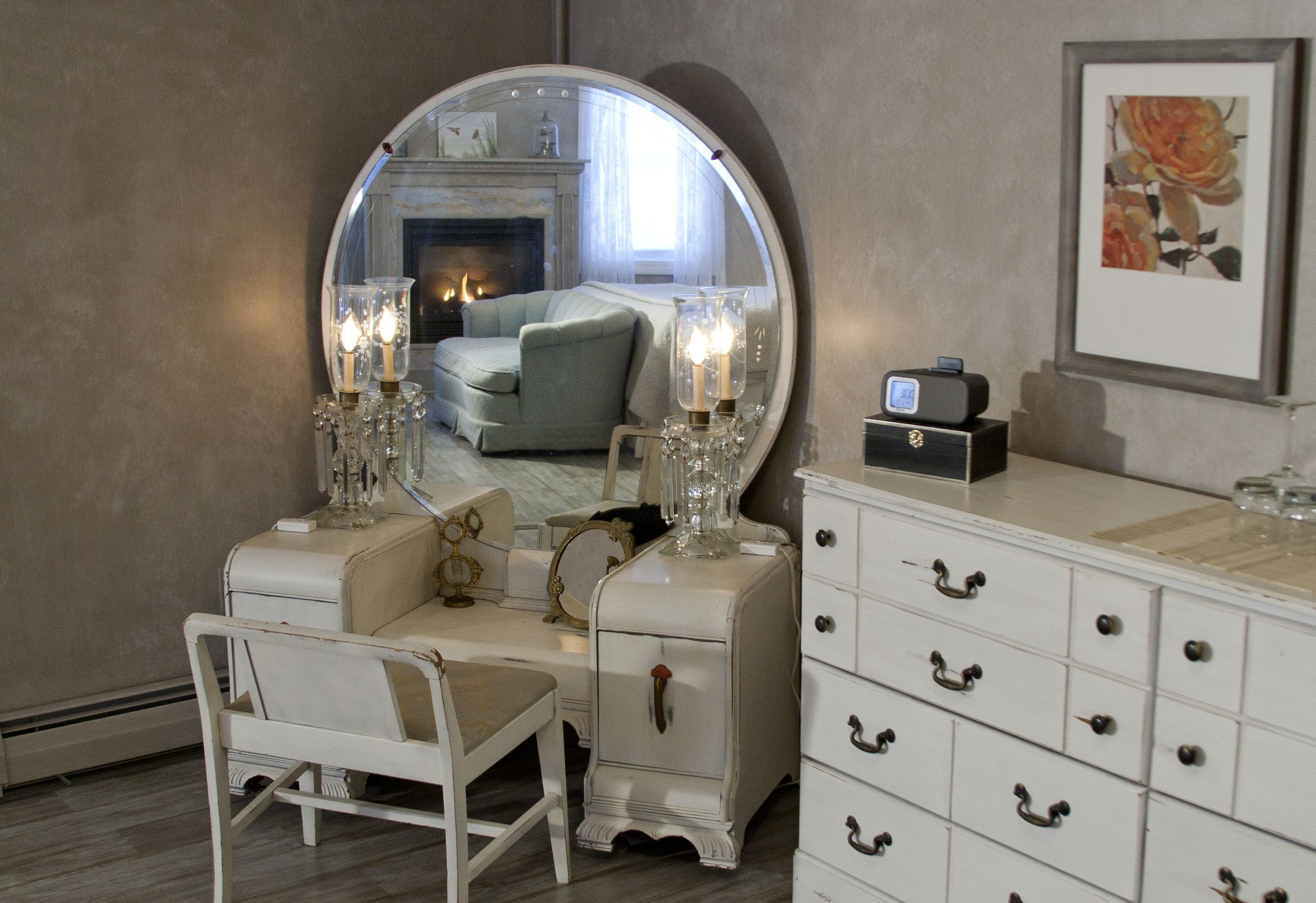 A room with a round mirror, a vanity with a dresser, and a chair.