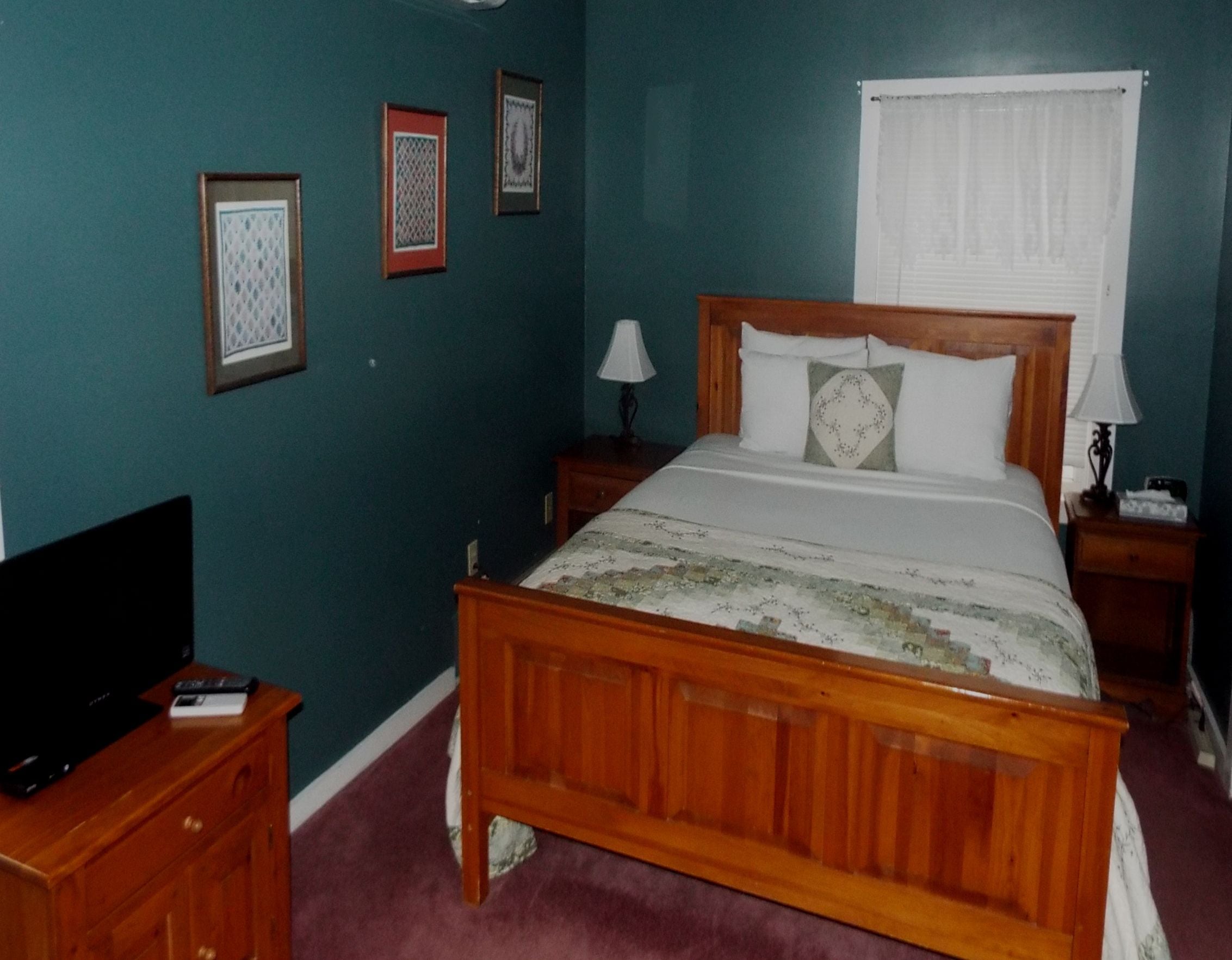 A bedroom with a wooden bed, a television on a nightstand, and a window with blinds.