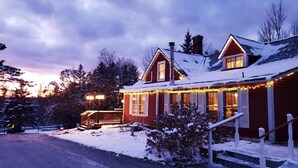 A two-story house with a snow-covered roof and front porch, featuring a staircase and a small garden area.