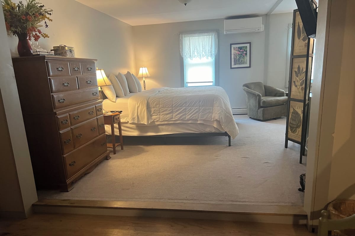 Quarto com cama, penteadeira, luminárias e uma cadeira.